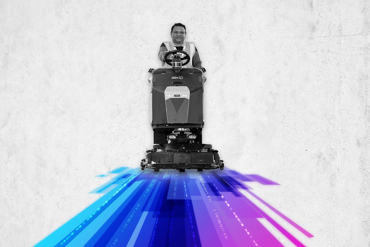 A Mitie colleague in black and white on a ride-on cleaner, with stripes of purple, blue and magenta underneath them